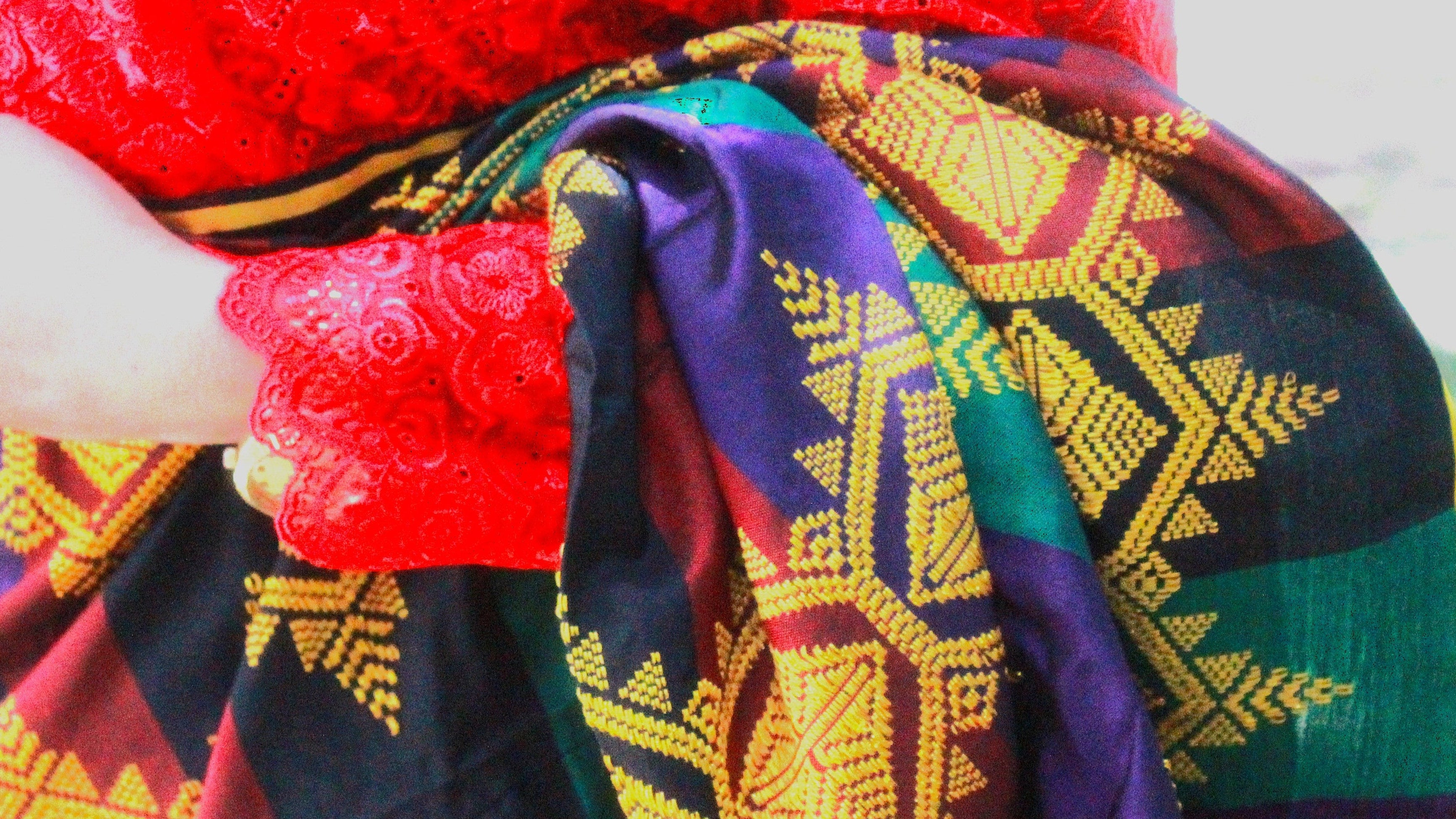 Colorful patterned fabric draped over a person wearing a red garment, with a blurred natural background.